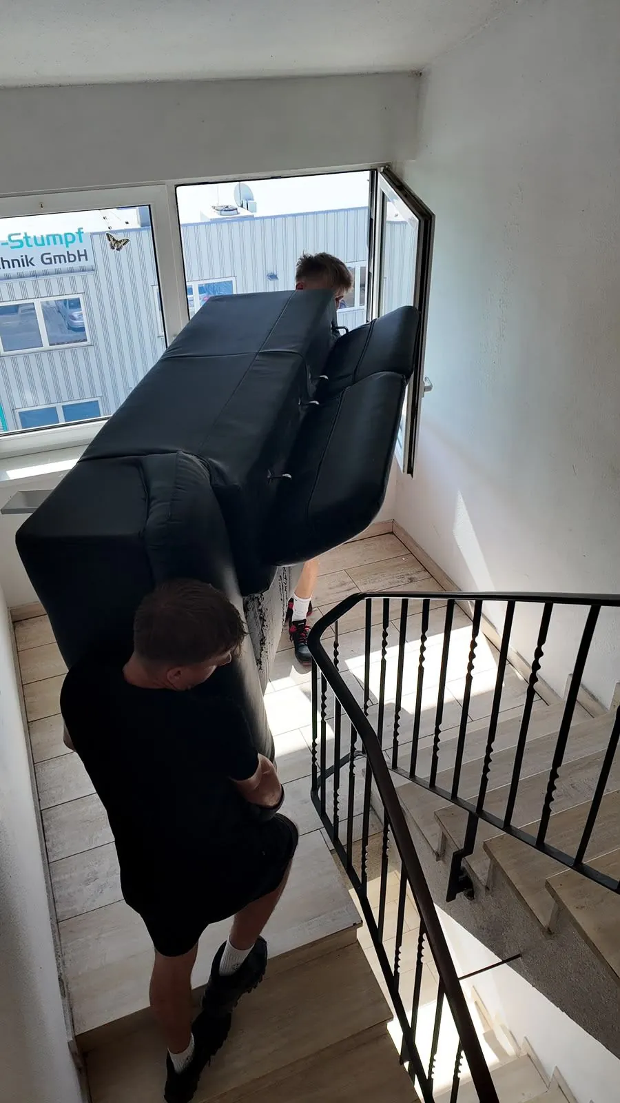 Zwei L&W-Mitarbeiter tragen ein Sofa durchs Treppenhaus